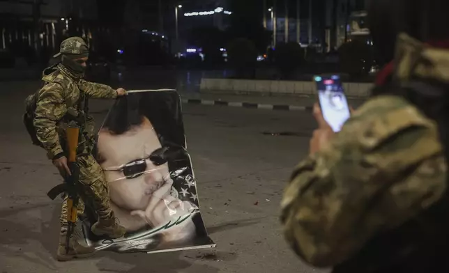 A Syrian opposition fighter takes a picture of a comrade stepping on a portrait of Syrian President Bashar Assad in Aleppo, early Saturday Nov. 30, 2024. (AP Photo/Ghaith Alsayed)