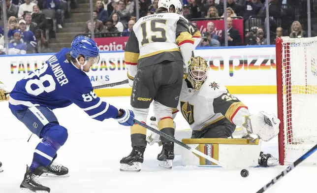 Toronto Maple Leafs' William Nylander (88) takes a shot on Vegas Golden Knights' goaltender Adin Hill (33) as Knights defenseman Noah Hanifin (15) looks for the rebound during second period NHL hockey action in Toronto, on Wednesday, November 20, 2024. (Chris Young/The Canadian Press via AP)