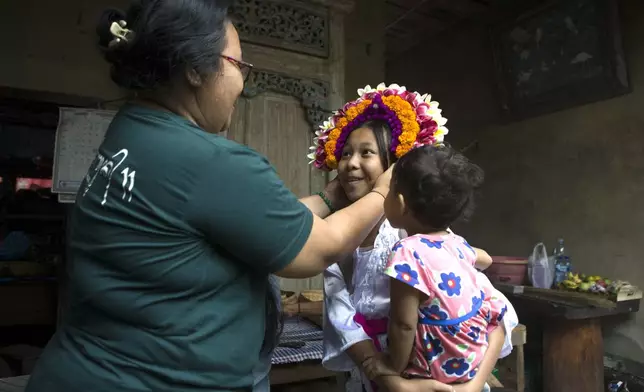 Kadek Krisni, left, tries on a headgear for size on her daughter Kadek Nita Wahyuni in preparation for a Hindu ritual at Geriana Kauh village, Karangasem, Bali, Indonesia on Thursday, Nov. 21, 2024. (AP Photo/Firdia Lisnawati)