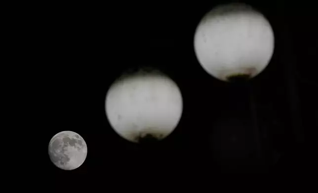 The moon rises behind street lamps in Milan, Italy, Thursday, Nov. 14, 2024. (AP Photo/Luca Bruno)