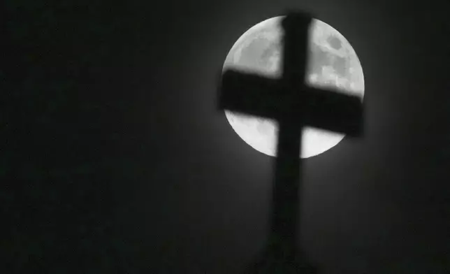 The moon rises behind the cross on top of St Paul's Church in Ealing, London, Friday, Nov. 15, 2024. (AP Photo/Frank Augstein)