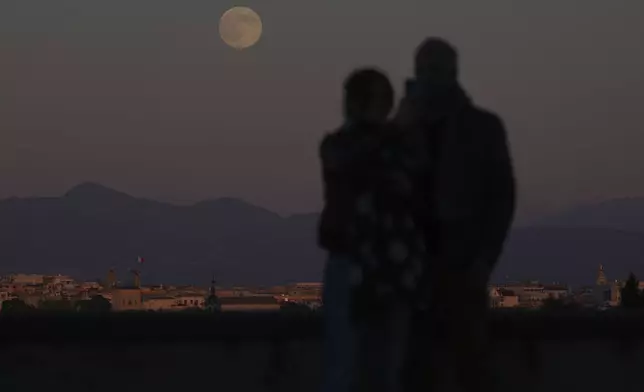 People watch at the full moon rising over Rome, Friday, Nov. 15, 2024. (AP Photo/Alessandra Tarantino)