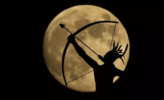 A bronze sculpture of "Ad Astra" a Kansa Indian, perched atop the Kansas Capitol dome is silhouetted against the nearly full moon Thursday, Nov. 14, 2024, on the eve of the final supermoon of the year in Topeka, Kan. (AP Photo/Charlie Riedel)