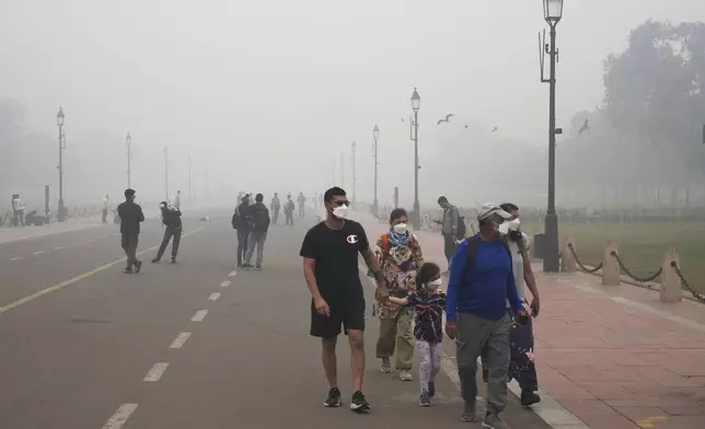 A foreign tourist family walks wearing face mask amidst a thick layer of smog as air pollution shoots up in New Delhi, India, Monday, Nov. 18, 2024. (AP Photo/Manish Swarup)