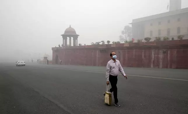 A office goer walks wearing a face mask amidst a thick layer of smog as air pollution shoots up in New Delhi, India, Monday, Nov. 18, 2024. (AP Photo/Manish Swarup)