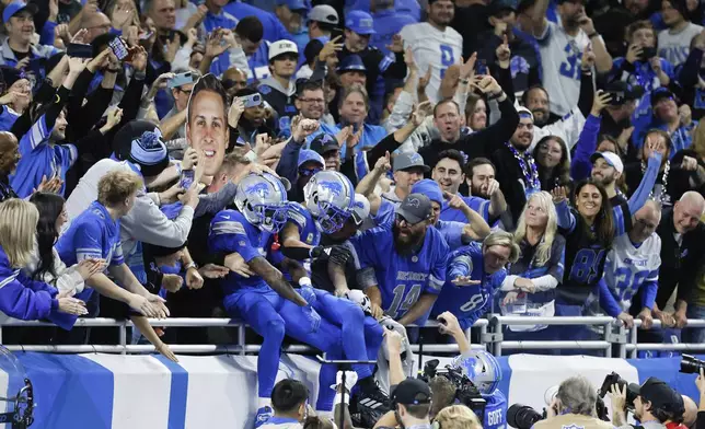 Detroit Lions wide receiver Amon-Ra St. Brown (14) celebrates his nine-yard touchdown reception with Jameson Williams (9) and quarterback Jared Goff (16) amongst fans during the second half of an NFL football game against the Jacksonville Jaguars, Sunday, Nov. 17, 2024, in Detroit. (AP Photo/Duane Burleson)