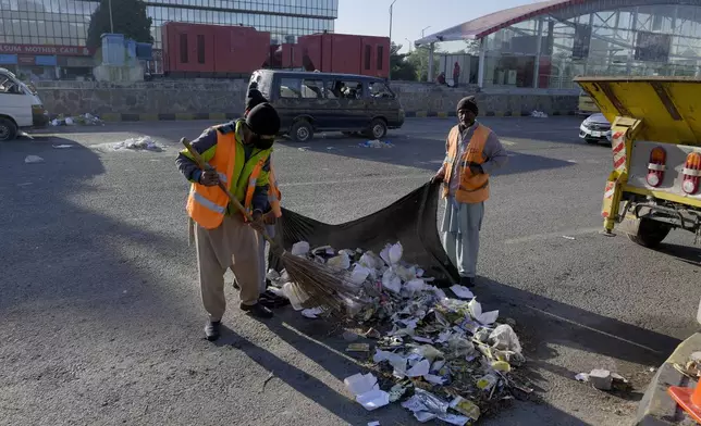 Workers clean an area near the damaged vehicles left behind by supporters of imprisoned former Prime Minister Imran Khan's Pakistan Tehreek-e-Insaf party when security forces launched an operation Tuesday night to disperse them, in Islamabad, Pakistan, Wednesday, Nov. 27, 2024. (AP Photo/Anjum Naveed)