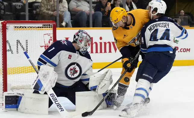 Winnipeg Jets goaltender Eric Comrie (1) reaches for a shot as Jets' Josh Morrissey (44) and Nashville Predators' Alexandre Carrier (45) battle in front of the net during the second period of an NHL hockey game Saturday, Nov. 23, 2024, in Nashville, Tenn. (AP Photo/Mark Humphrey)