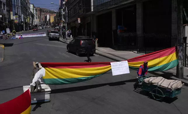 FILE - Meat vendors block a street with a Bolivian national flag near the market that they closed down for their 24-hour strike against inflation and to demand the government control border smuggling, in La Paz, Bolivia, Oct. 21, 2024. (AP Photo/Juan Karita)