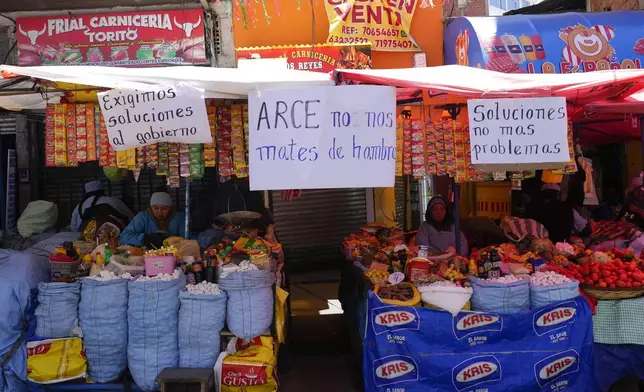 FILE - Handwritten sign with messages that read in Spanish: "We demand solutions from the government", "Arce, don't starve us" and "Solutions, not more problems", hang from vendors' stalls at a street market in La Paz, Bolivia, Oct. 21, 2024. (AP Photo/Juan Karita, File)