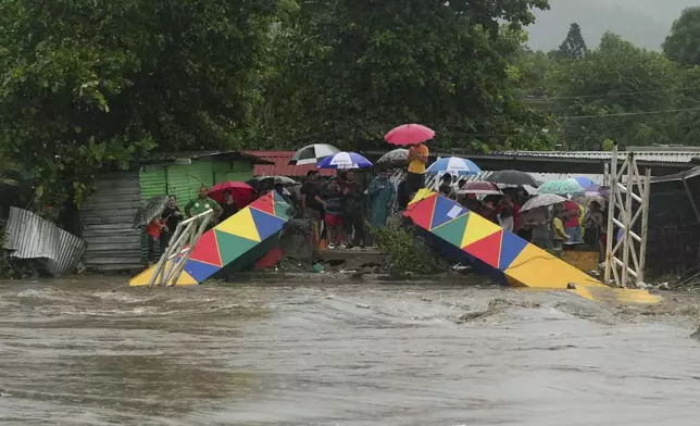 People stand at alongside a pedestrian bridge collapsed due to flooding caused by rains brought on by Tropical Storm Sara in San Pedro Sula, Honduras Saturday, Nov. 16, 2024. (AP Photo/Moises Castillo)