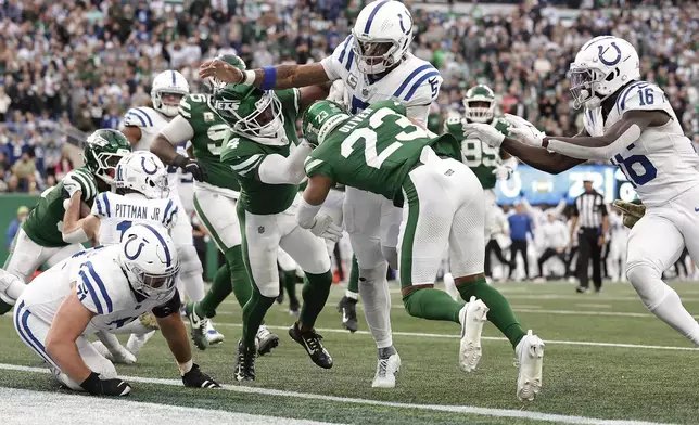 Indianapolis Colts quarterback Anthony Richardson (5) breaks through tackles by New York Jets cornerback Isaiah Oliver (23) and cornerback D.J. Reed (4) to score a touchdown during the fourth quarter of an NFL football game, Sunday, Nov. 17, 2024, in East Rutherford, N.J. (AP Photo/Adam Hunger)