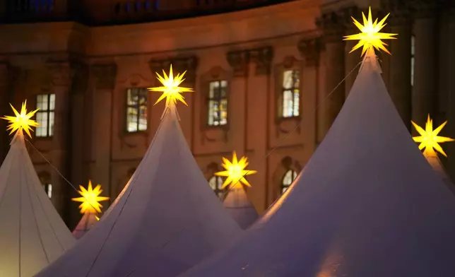 Christmas stars illuminate the top of the tents of the Christmas market at Bebelplatz in the city center of Berlin, Germany, Monday, Nov. 25, 2024. (AP Photo/Markus Schreiber)