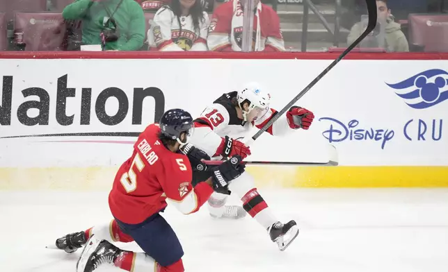 Florida Panthers defenseman Aaron Ekblad (5) and New Jersey Devils center Nico Hischier (13) battle for the puck during the first period of an NHL hockey game, Thursday, Nov. 14, 2024, in Sunrise, Fla. (AP Photo/Wilfredo Lee)