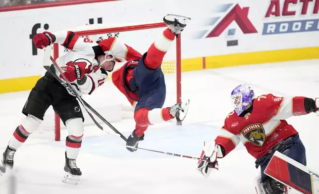 Florida Panthers defenseman Nate Schmidt, center, goes airborne as he and goaltender Sergei Bobrovsky, right, protect the net against New Jersey Devils left wing Ondrej Palat (18) during the second period of an NHL hockey game, Thursday, Nov. 14, 2024, in Sunrise, Fla. (AP Photo/Wilfredo Lee)