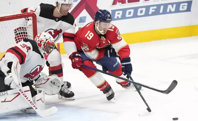 Florida Panthers left wing Matthew Tkachuk (19) attempts to score against New Jersey Devils goaltender Jake Allen (34) and defenseman Dougie Hamilton (7) during the first period of an NHL hockey game, Thursday, Nov. 14, 2024, in Sunrise, Fla. (AP Photo/Wilfredo Lee)