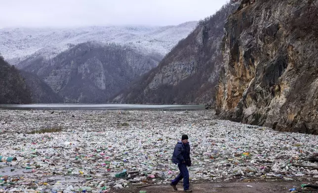 FILE- A man walks past waste floating in the Drina river near Visegrad, Bosnia, Jan. 10, 2024. (AP Photo/Armin Durgut, File)