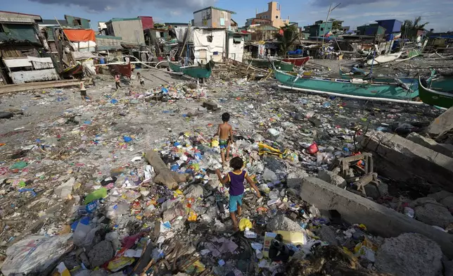 Children walk along debris, including plastics, that was washed ashore from previous typhoons along a bayside slum area on Tuesday, Nov. 26, 2024, in Navotas, Philippines. (AP Photo/Aaron Favila)