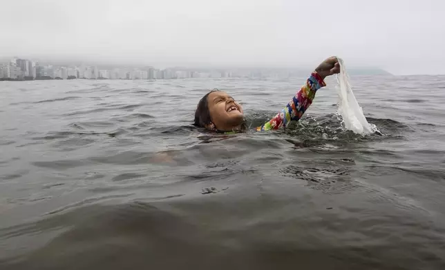 FILE- Nina Gomes recovers a discarded plastic bag from ocean waters, near Copacabana beach in Rio de Janeiro, Brazil, March 19, 2024. (AP Photo/Bruna Prado, File)