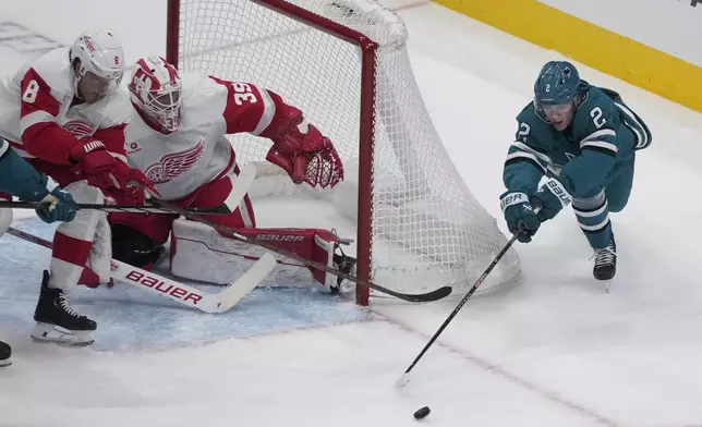 San Jose Sharks center Will Smith (2) reaches for the puck against Detroit Red Wings defenseman Ben Chiarot (8) and goaltender Cam Talbot (39) during the third period of an NHL hockey game in San Jose, Calif., Monday, Nov. 18, 2024. (AP Photo/Jeff Chiu)