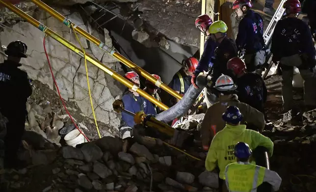 Construction workers, along with members of the Louisville Metro Fire Department, use a large vacuum to remove debris as they attempt to rescue a worker trapped underground at a construction site in Louisville, Ky., Thursday, Nov. 14, 2024. (AP Photo/Timothy D. Easley)