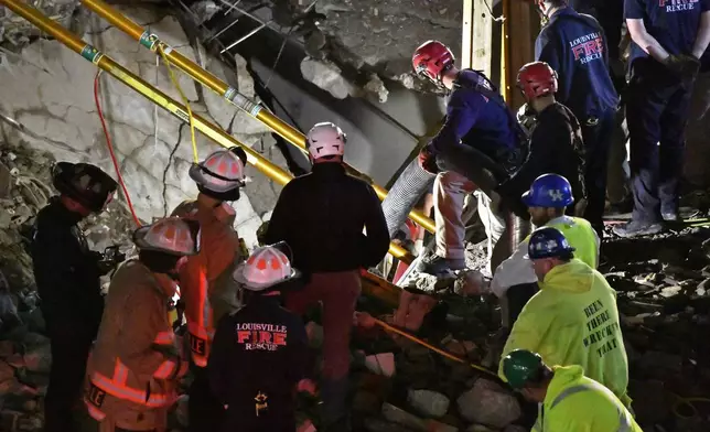 Construction workers and members of the Louisville Metro Fire Department use a large vacuum to remove debris as they attempt to rescue a worker trapped underground at a construction site in Louisville, Ky., Thursday, Nov. 14, 2024. (AP Photo/Timothy D. Easley)