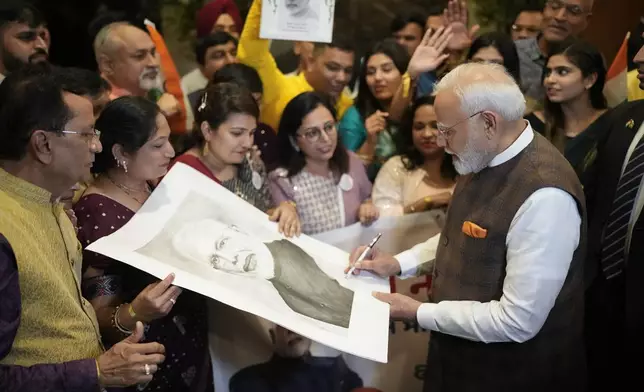 India's Prime Minister Narendra Modi signs a portrait of himself for a member of Guyana's Hindu community as he arrives to his hotel in Georgetown, Guyana, Tuesday, Nov. 19, 2024. (AP Photo/Matias Delacroix)