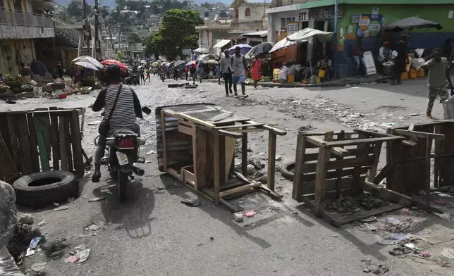 A motorcycle taxi driver crosses a barricade set up by residents, in Port-au-Prince, Haiti, Thursday, Nov. 14, 2024. (AP Photo/Odelyn Joseph)