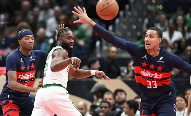 Boston Celtics guard Jaylen Brown, center, passes the ball off against Washington Wizards guard Bilal Coulibaly, left, and Wizards forward Kyle Kuzma (33) during the first half of an Emirates NBA Cup basketball game Friday, Nov. 22, 2024, in Washington. (AP Photo/John McDonnell)