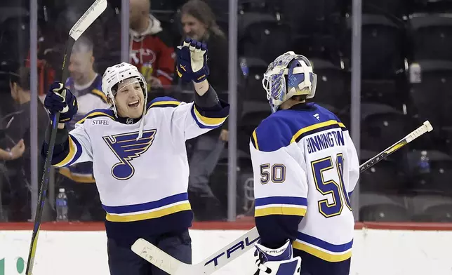 St. Louis Blues left wing Jake Neighbours reacts towards goaltender Jordan Binnington (50) after beating the New Jersey Devils 3-0 in an NHL hockey game Wednesday, Nov. 27, 2024, in Newark, N.J. St. (AP Photo/Adam Hunger)