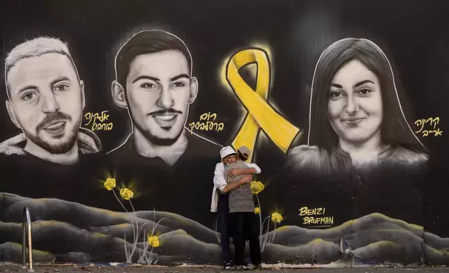 People hug next to graffiti portraits of Gaza-held hostages in Jerusalem, Friday, Nov. 22, 2024. (AP Photo/Ohad Zwigenberg)