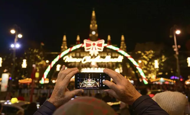 A man takes photographs of the illuminations at the Wiener Chritkindlmarkt in front of Vienna's city hall, one of Vienna's most popular Christmas markets, in Vienna, Austria, Saturday, Nov. 16, 2024. (AP Photo/Christian Bruna)