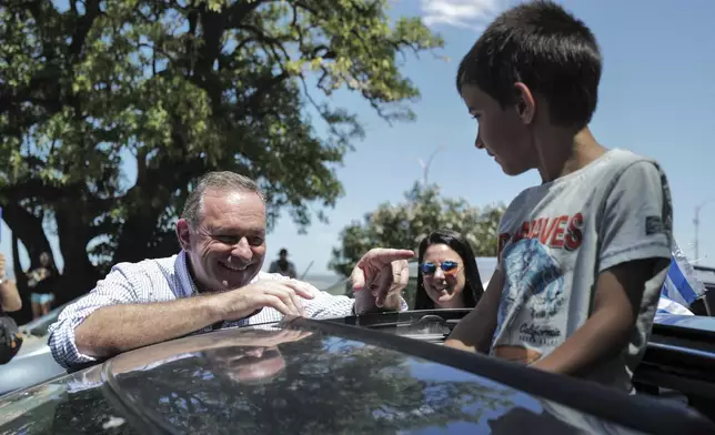 Alvaro Delgado, candidate for the ruling National Party, talks to a boy after voting in the presidential run-off election in Montevideo, Uruguay, Sunday, Nov. 24, 2024. (AP Photo/Jon Orbach)