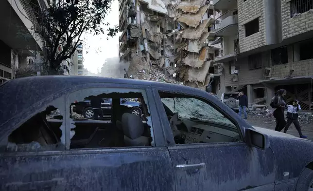 Residents pass in front of a destroyed building that was hit Sunday night in an Israeli airstrike in Dahiyeh, in the southern suburb of Beirut, Lebanon, Monday, Nov. 25, 2024. (AP Photo/Hussein Malla)