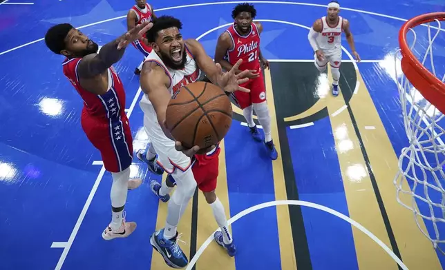 New York Knicks' Karl-Anthony Towns, center, goes up for a shot past Philadelphia 76ers' Paul George, left, during the second half of an Emirates NBA Cup basketball game, Tuesday, Nov. 12, 2024, in Philadelphia. (AP Photo/Matt Slocum)