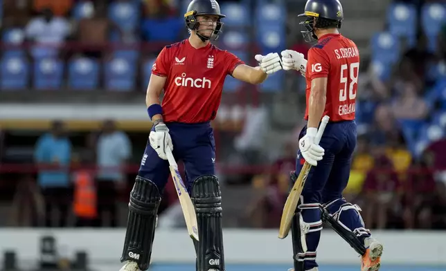 England's Jordan Cox celebrates with teammate Sam Curran his third six in a row from the bowling of West Indies' Roston Chase during the fourth T20 cricket match at Daren Sammy National Cricket Stadium in Gros Islet, St. Lucia, Saturday, Nov. 16, 2024. (AP Photo/Ricardo Mazalan)