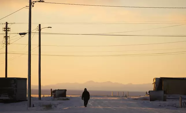 A resident walks up a street as the sun rises Tuesday, Oct. 15, 2024, in Kaktovik, Alaska. (AP Photo/Lindsey Wasson)