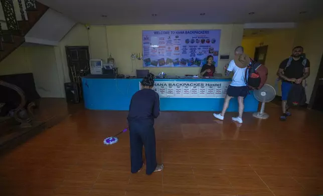 A woman swipes the floor as foreign tourists check out of Nana Backpack hostel in Vang Vieng, Laos, Tuesday, Nov. 19, 2024. (AP Photo/Anupam Nath)