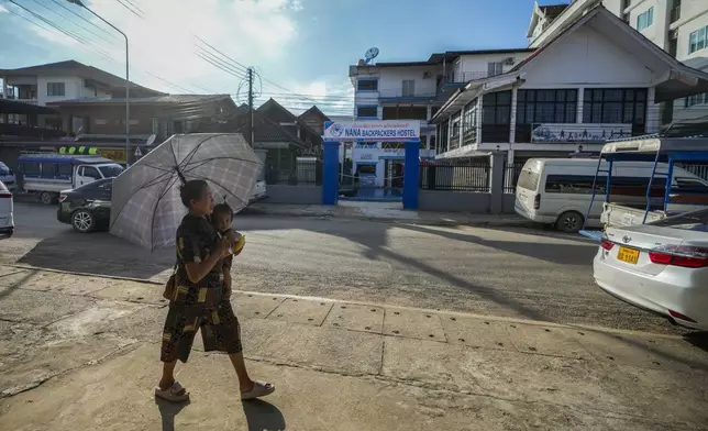 A woman carries a baby as she walks by the Nana Backpack hostel in Vang Vieng, Laos, Tuesday, Nov. 19, 2024. (AP Photo/Anupam Nath)