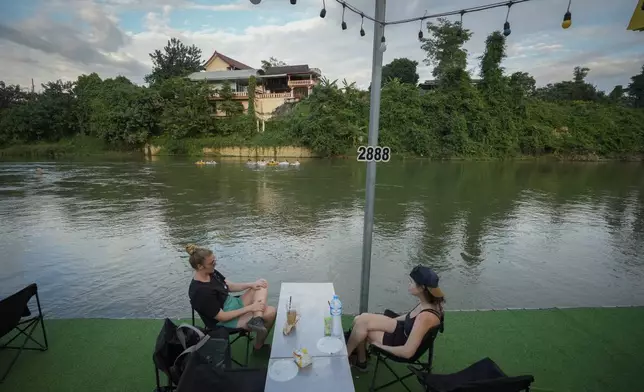 Foreign tourists drink beer at a bar near a river in Vang Vieng, Laos, Tuesday, Nov. 19, 2024. (AP Photo/Anupam Nath)