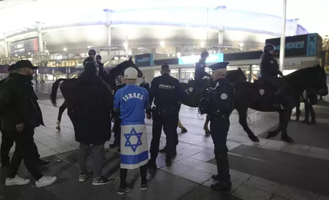 Police check a man covered with an Israeli flag next to the Stade de France before the UEFA Nations League soccer match between France and Israel, in Saint-Denis, outside Paris, Thursday, Nov. 14, 2024. (AP Photo/Thibault Camus)