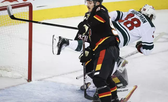 Minnesota Wild's Ryan Hartman, right, is checked into by Calgary Flames goalie Dustin Wolf, hidden, by Brayden Pachal during second period NHL hockey action in Calgary on Saturday, Nov. 23, 2024. (Jeff McIntosh/The Canadian Press via AP)