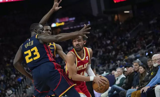 Atlanta Hawks guard Trae Young, right, looks for an open teammate while defended by Golden State Warriors forwards Draymond Green, left, and Andrew Wiggins during the first half of an NBA basketball game Wednesday, Nov. 20, 2024, in San Francisco. (AP Photo/Godofredo A. Vásquez)