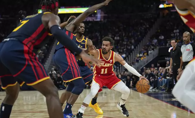 Atlanta Hawks guard Trae Young (11) looks for an open teammate while defended by Golden State Warriors forwards Draymond Green, second from left, and Andrew Wiggins during the first half of an NBA basketball game Wednesday, Nov. 20, 2024, in San Francisco. (AP Photo/Godofredo A. Vásquez)