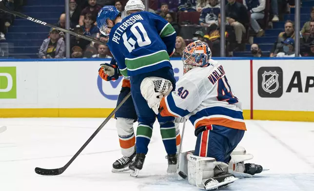 New York Islanders' goalie Semyon Varlamov, right, makes a save with Vancouver Canucks' Elias Pettersson, front left, screening during second-period NHL hockey game action in Vancouver, British Columbia, Thursday, Nov. 14, 2024.(Rich Lam/The Canadian Press via AP)