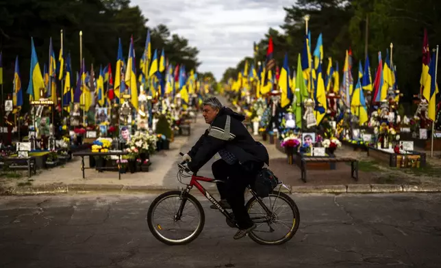 FILE - A man rides a bicycle past the tombs of Ukrainian soldiers killed during the war, at Lisove cemetery in Kyiv, Ukraine, on April 23, 2024. (AP Photo/Francisco Seco, File)