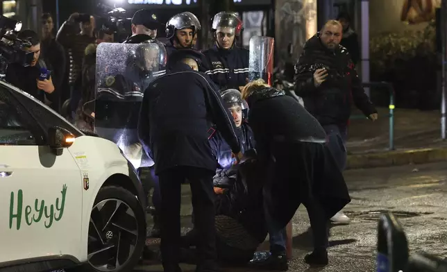 Police officers help a woman after a clash between riot police and opposition supporters in Tirana, Albania, Tuesday, Nov. 26, 2024 during an anti-government protest over the arrests of their leader Sali Berisha and former President Ilir Meta in separate corruption cases, saying the charges are politically motivated. (AP Photo/Vlasov Sulaj)