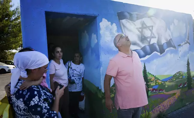 People take cover next to a public bomb shelter as a siren sounds a warning of incoming rockets fired from Lebanon, in Safed, northern Israel, Sunday, Sept. 29, 2024. (AP Photo/Ariel Schalit)