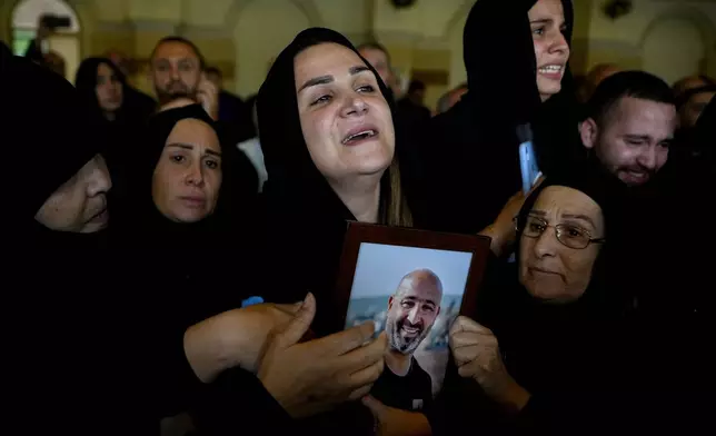 Manal Jaafar, centre. reacts as she hugs a photo of her husband Rabih Maamari, a cameraman at pan-Arab TV network Al-Mayadeen who was killed by an Israeli strike, during his funeral procession in the southern Beirut suburb of Dahiyeh, Lebanon, Wednesday, Nov. 22, 2023. (AP Photo/Bilal Hussein)