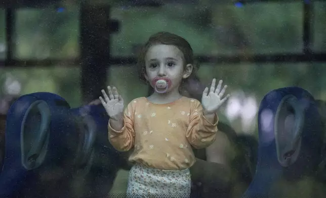 A young girl looks through a bus window as her family departs the northern Israeli city of Kiryat Shmona, Israel, Friday, Oct. 20, 2023 after the Israeli military announced it would evacuate the border city a day after three residents were injured by cross-border fire from militants in Lebanon. (AP Photo/Baz Ratner)